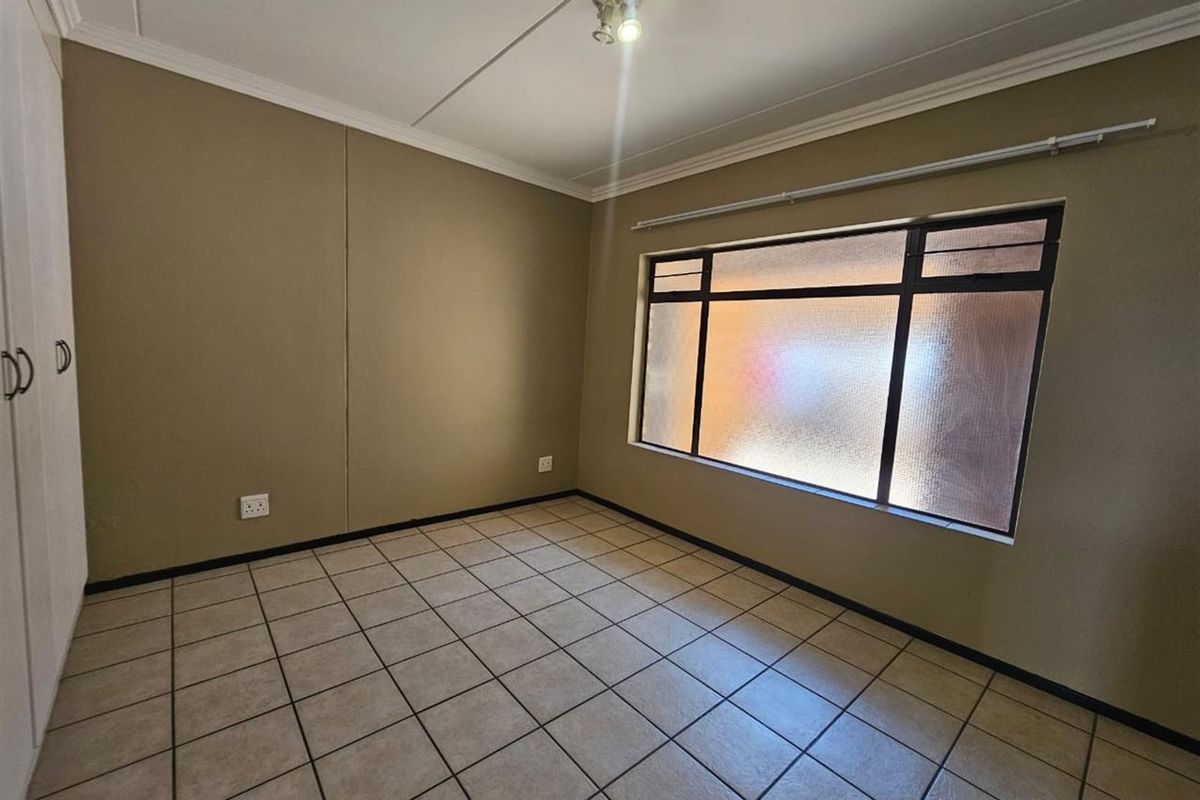An empty bedroom featuring tiled flooring, built-in cupboards, and a large window with textured glass, providing a neutral canvas for personalization.