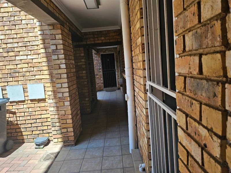 A covered outdoor walkway featuring face brick walls, tiled flooring, and a security gate, providing access to the townhouse entrance.