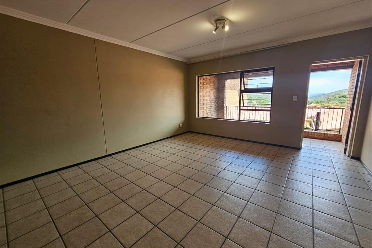 An empty, tiled living room featuring neutral walls, a ceiling light fixture, and direct access to an outdoor balcony with scenic views.