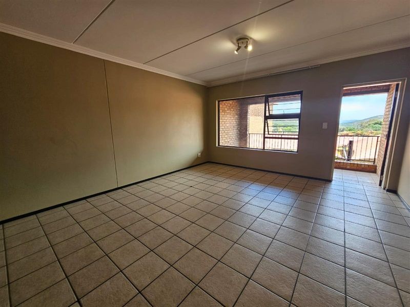 An empty, tiled living room featuring neutral walls, a ceiling light fixture, and direct access to an outdoor balcony with scenic views.