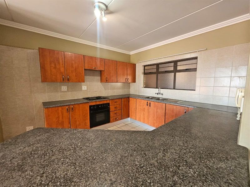 A functional kitchen featuring wooden cabinetry, granite countertops, a built-in oven and hob, and a double sink with tiled backsplash.