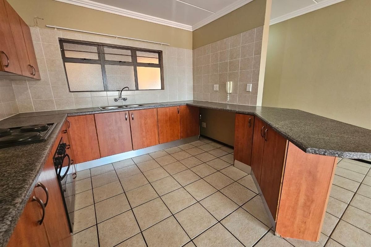 A functional kitchen featuring wood-look cabinetry, granite countertops, built-in oven and hob, and tiled flooring, offering a clean and practical workspace.