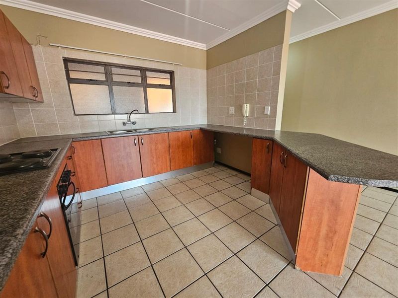 A functional kitchen featuring wood-look cabinetry, granite countertops, built-in oven and hob, and tiled flooring, offering a clean and practical workspace.
