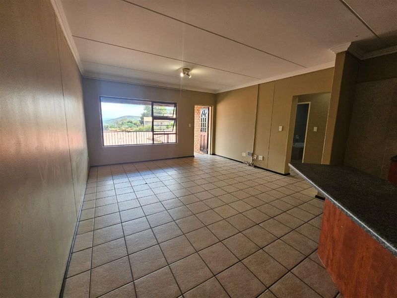 Spacious open-plan living area featuring tiled flooring, a breakfast bar, and access to an exterior door with security gate.