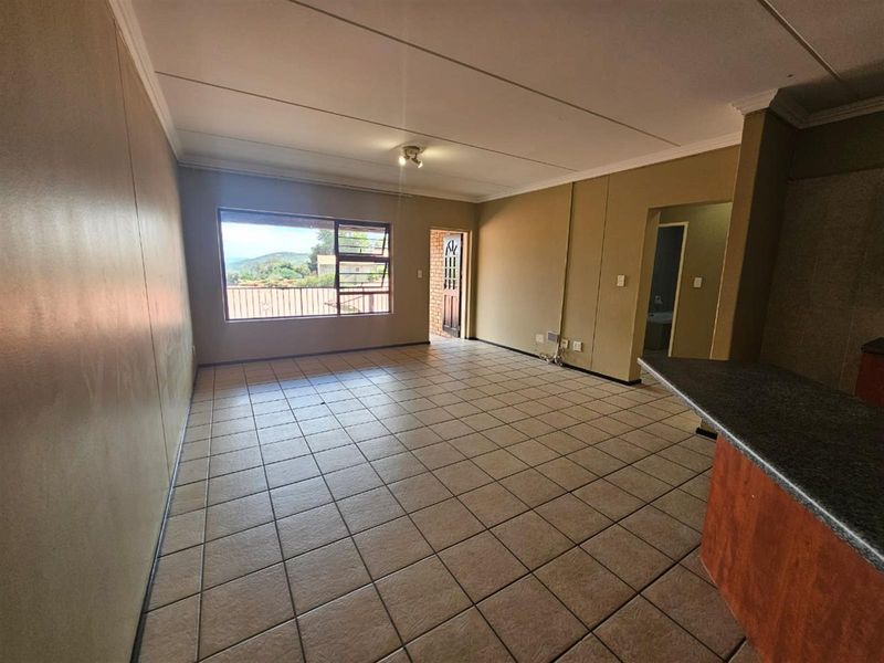 Spacious open-plan living area featuring tiled flooring, a breakfast bar, and access to an exterior balcony with scenic views.