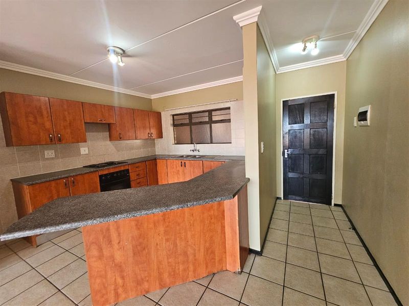A functional kitchen featuring wooden cabinetry, laminate countertops, built-in oven and hob, tiled backsplash, and tiled flooring.