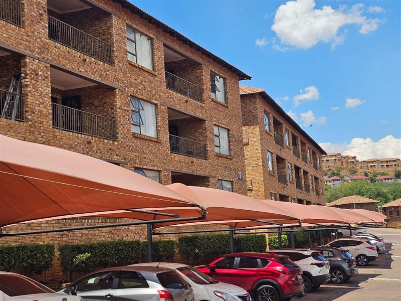 Exterior view of a multi-story face brick townhouse complex featuring private balconies and covered parking bays.