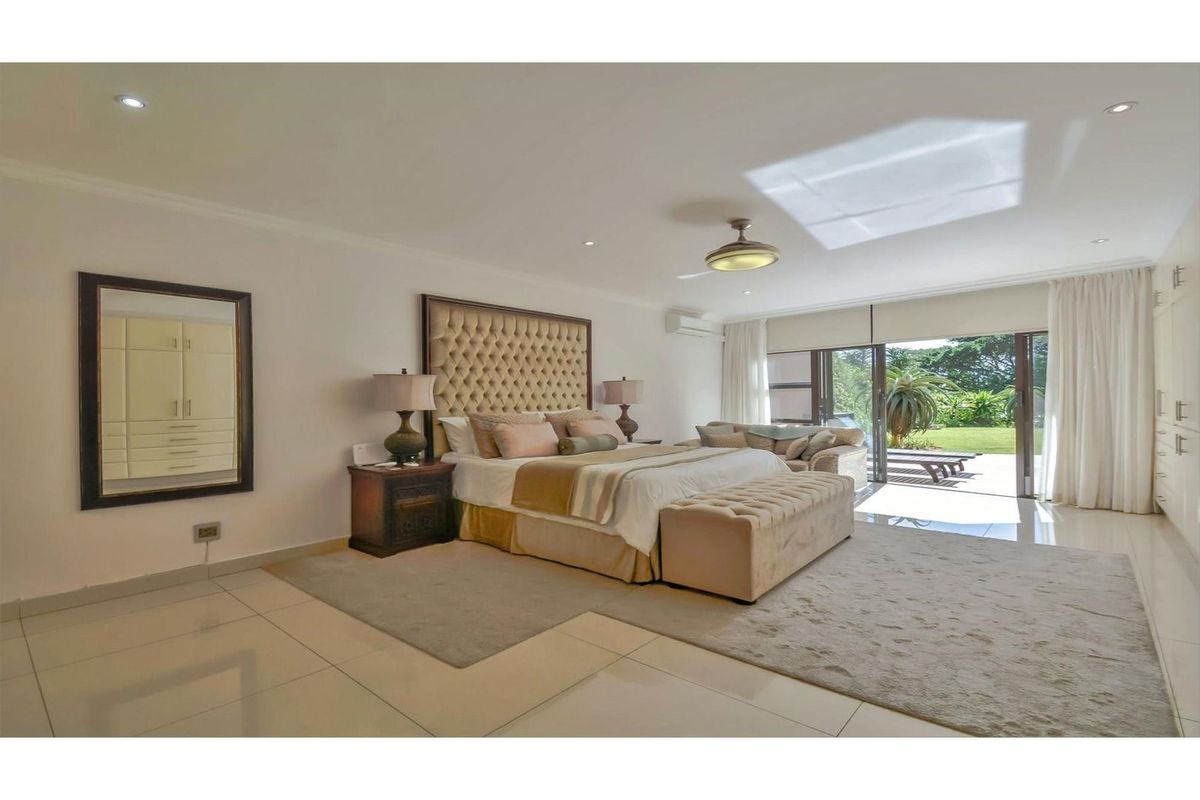 Spacious master bedroom featuring large format floor tiles, recessed downlighting, air conditioning unit, and sliding glass doors opening to a private garden patio.