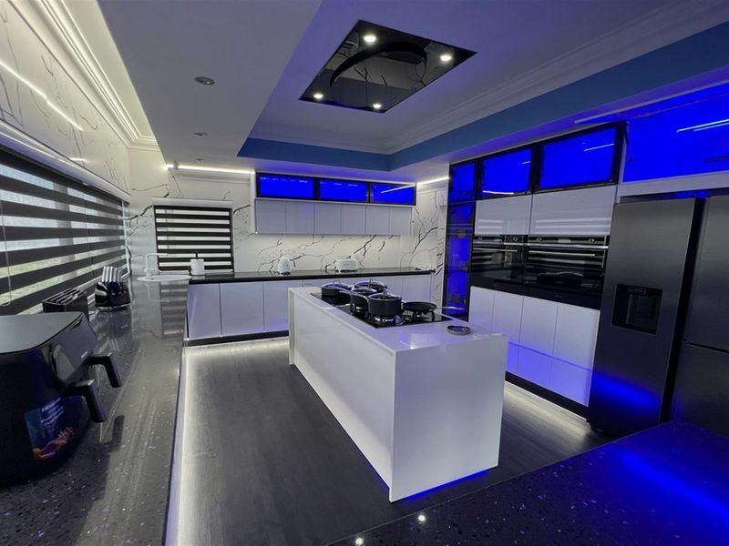 Modern kitchen featuring a central island with integrated cooktop, sleek cabinetry, built-in ovens, and ambient LED lighting throughout.