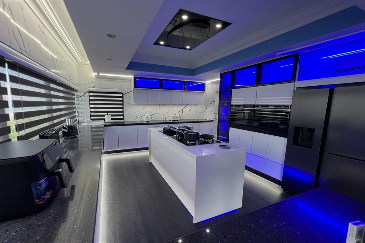 Modern kitchen featuring a central island with integrated cooktop, sleek cabinetry, built-in ovens, and ambient LED lighting throughout.