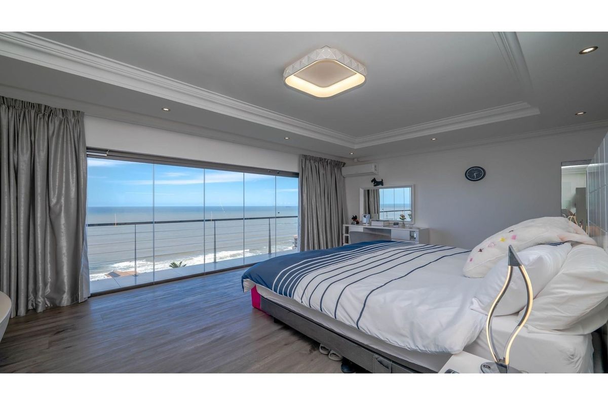 Spacious bedroom featuring modern recessed lighting, crown molding, wood-look flooring, and large floor-to-ceiling glass sliding doors opening to a scenic ocean-view balcony.