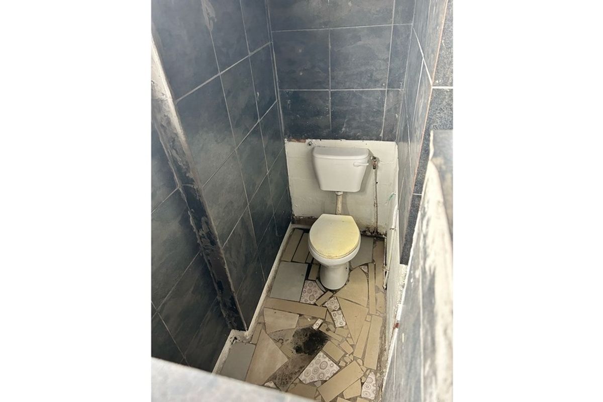 A small bathroom featuring dark wall tiling and a toilet, currently in need of significant repair and renovation due to damaged flooring and finishes.
