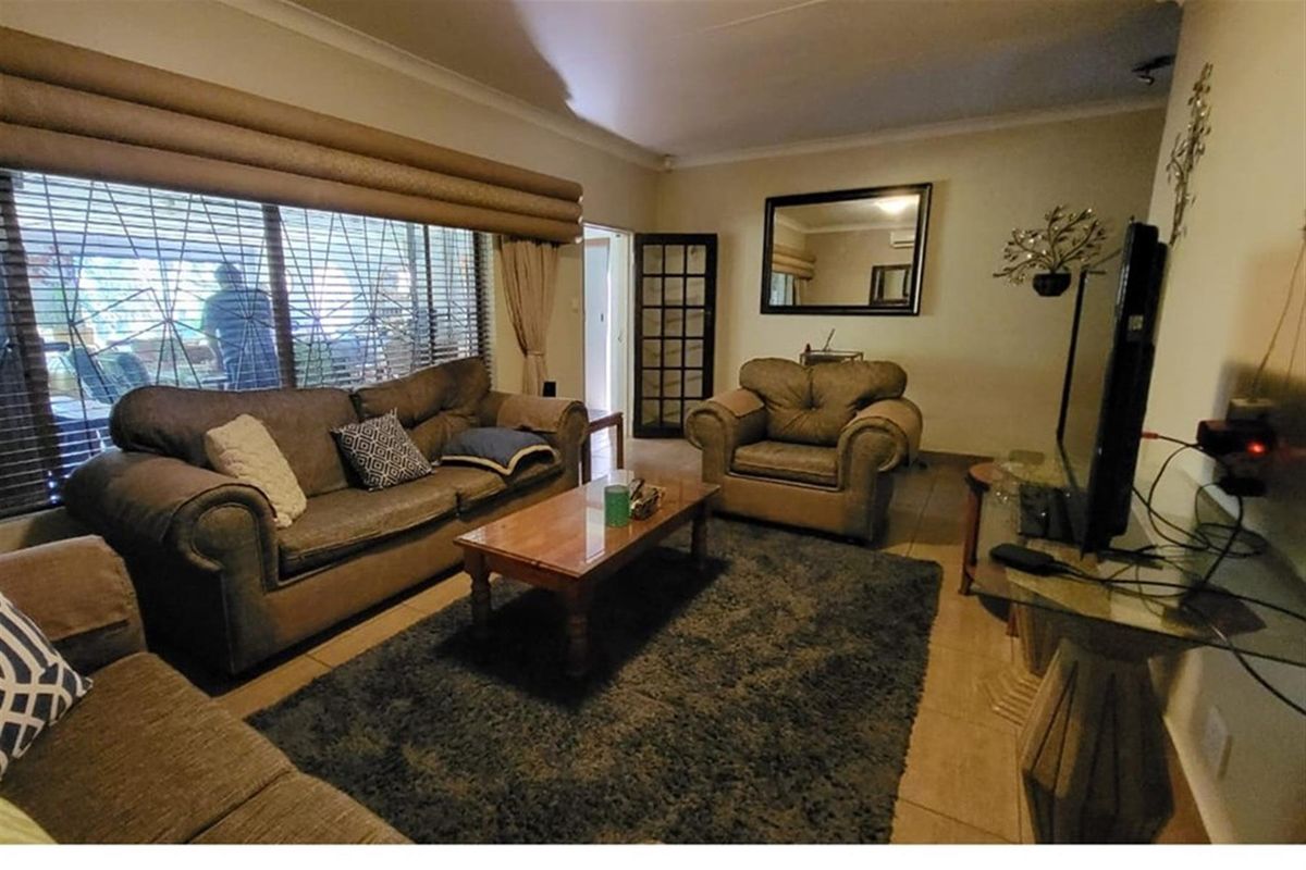 A comfortable living room featuring tiled flooring, large windows with fitted blinds, and a classic French door leading to the adjacent space.
