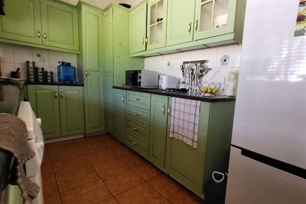 A functional kitchen featuring green cabinetry, dark countertops, and tiled flooring, providing a practical workspace for retail or office staff.