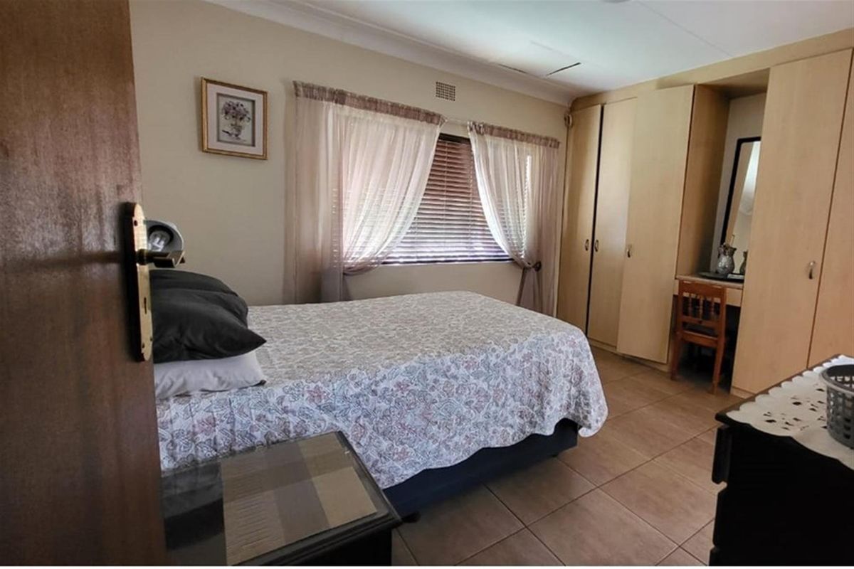 A bedroom featuring built-in wooden cabinetry, tiled flooring, and a window with fitted blinds and curtains.