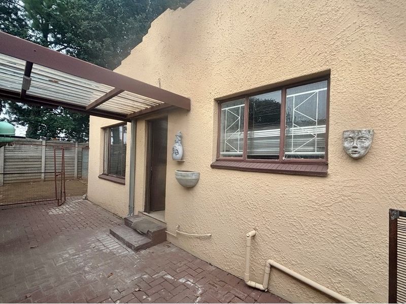 Rear exterior view of the cottage featuring a paved patio area, covered walkway, and textured stucco facade with security-fitted windows.