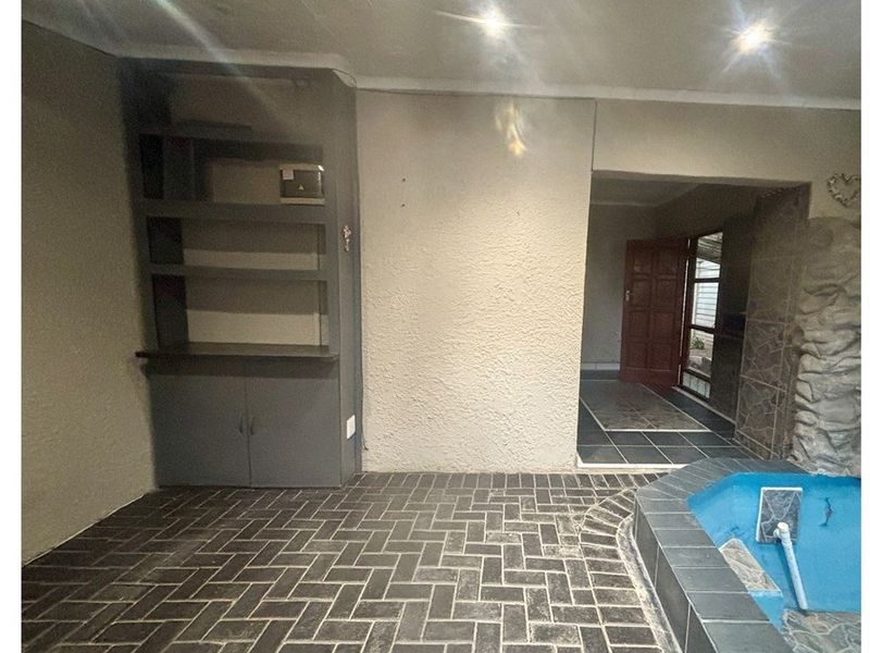 An indoor patio or entertainment area featuring built-in shelving, tiled flooring, and a small built-in water feature, offering potential for a cozy lounge space.