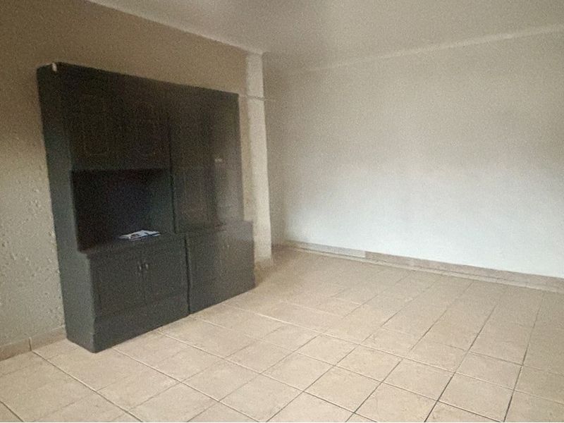 An empty living room featuring tiled flooring and built-in dark cabinetry, offering a blank canvas for renovation and interior design updates.