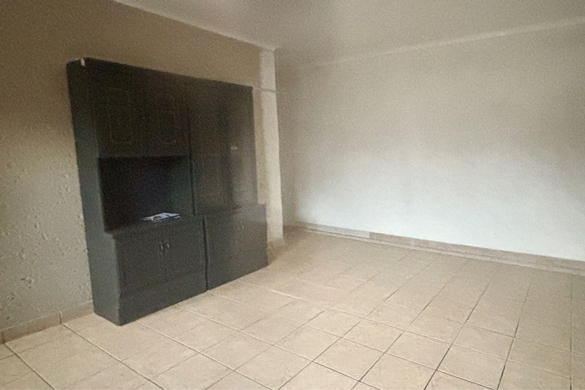 An empty living room featuring tiled flooring and built-in dark cabinetry, offering a blank canvas for renovation and interior design updates.