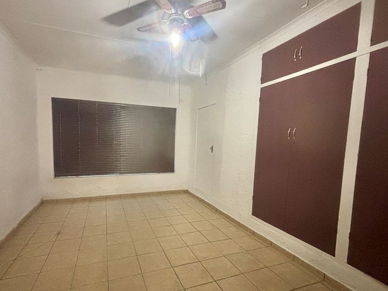 An empty bedroom featuring tiled flooring, a ceiling fan, and built-in cupboards with a dated finish.