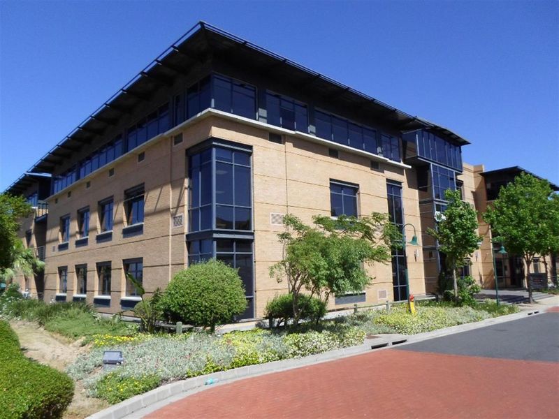 A modern commercial office building featuring a brick facade, extensive glass windows, and a prominent overhanging roof design with surrounding landscaped grounds.