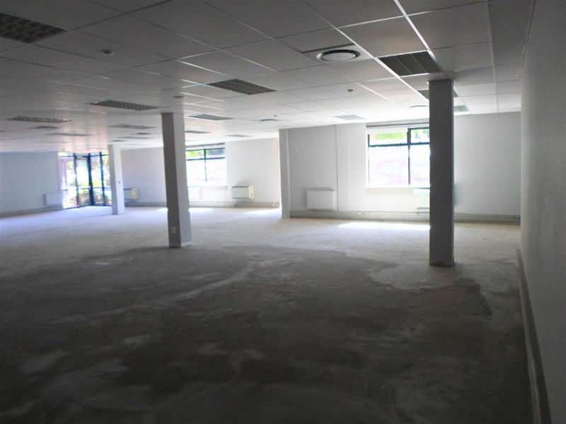 A large, open-plan commercial office space featuring a suspended ceiling, structural columns, and large windows, currently in a shell condition ready for fit-out.