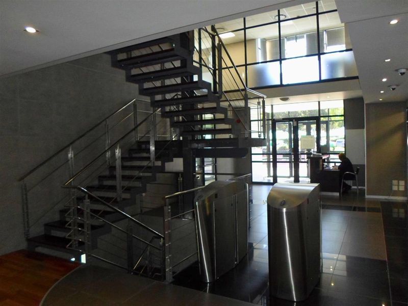 Modern commercial building entrance featuring an open-tread staircase, security turnstiles, and a glass facade providing ample natural light.