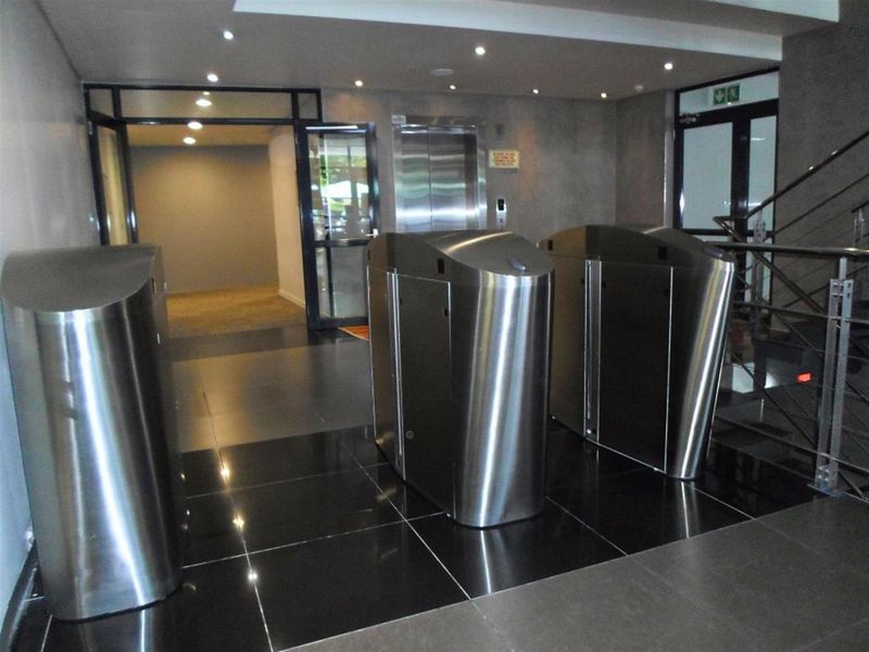 Modern commercial building entrance lobby featuring stainless steel security turnstiles, elevator access, and polished tiled flooring.