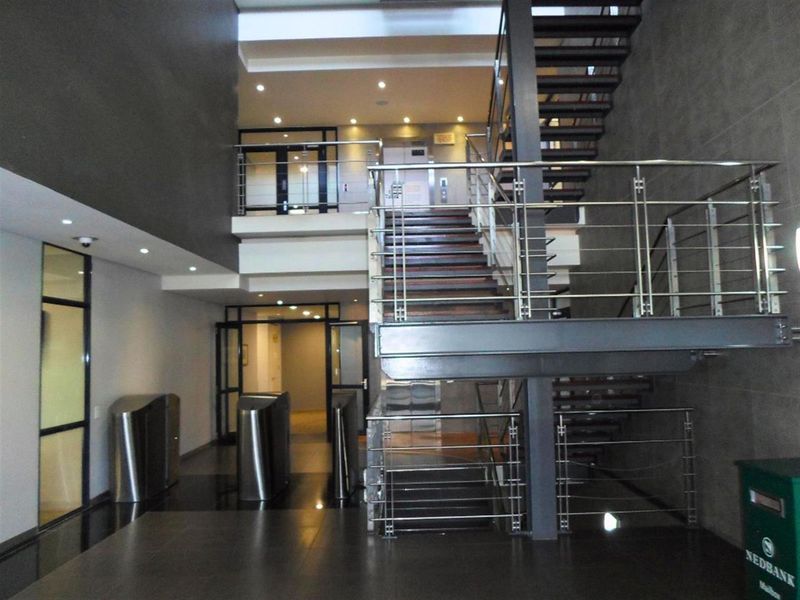 Modern commercial building entrance lobby featuring a prominent staircase with stainless steel balustrades, security turnstiles, and integrated elevator access.