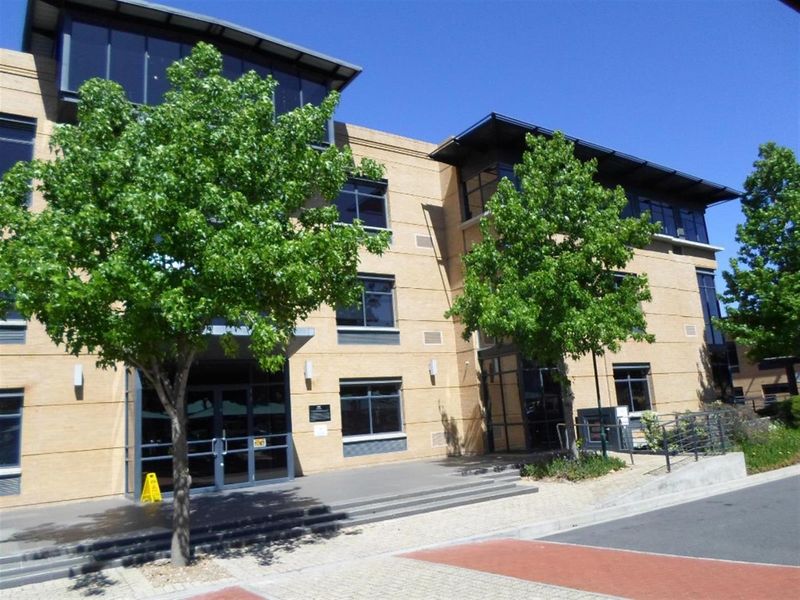 Front elevation of a multi-story commercial office building featuring brick cladding, large aluminum-framed windows, and a paved entrance area.