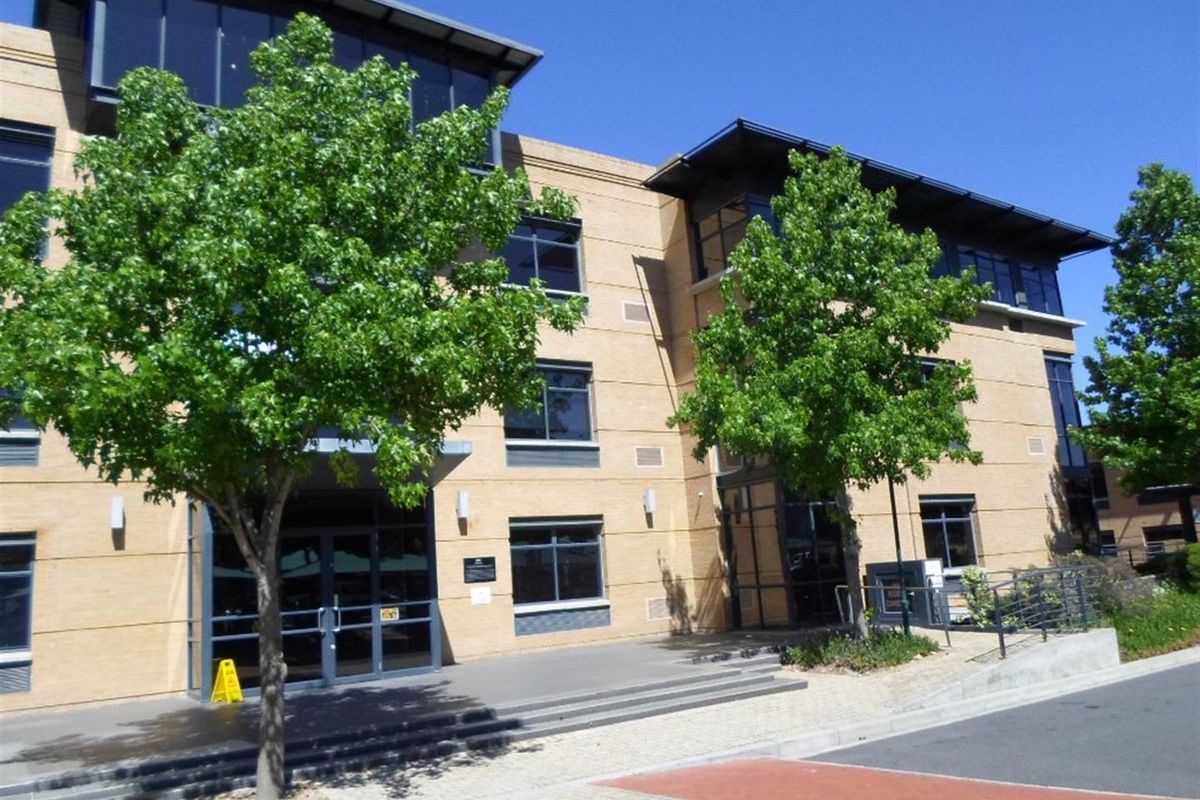 Front elevation of a multi-story commercial office building featuring brick cladding, large aluminum-framed windows, and a paved entrance area.