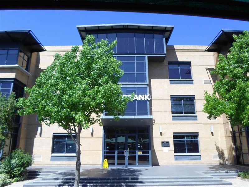 Front elevation of a multi-story commercial office building featuring a brick facade, large glass curtain wall, and a prominent glass entrance.