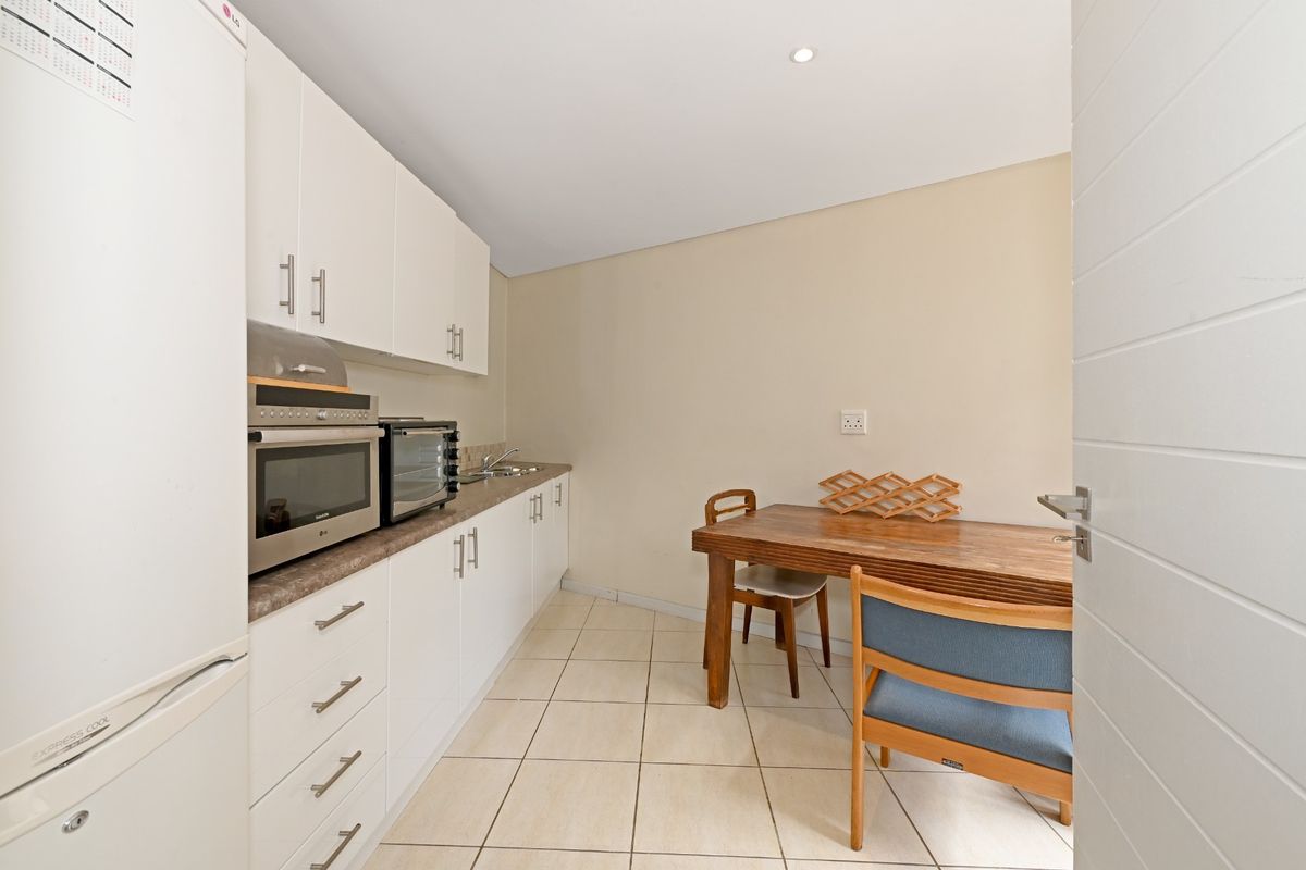 A compact kitchen featuring white cabinetry, laminate countertops, a stainless steel sink, and tiled flooring, providing a functional prep and dining space.