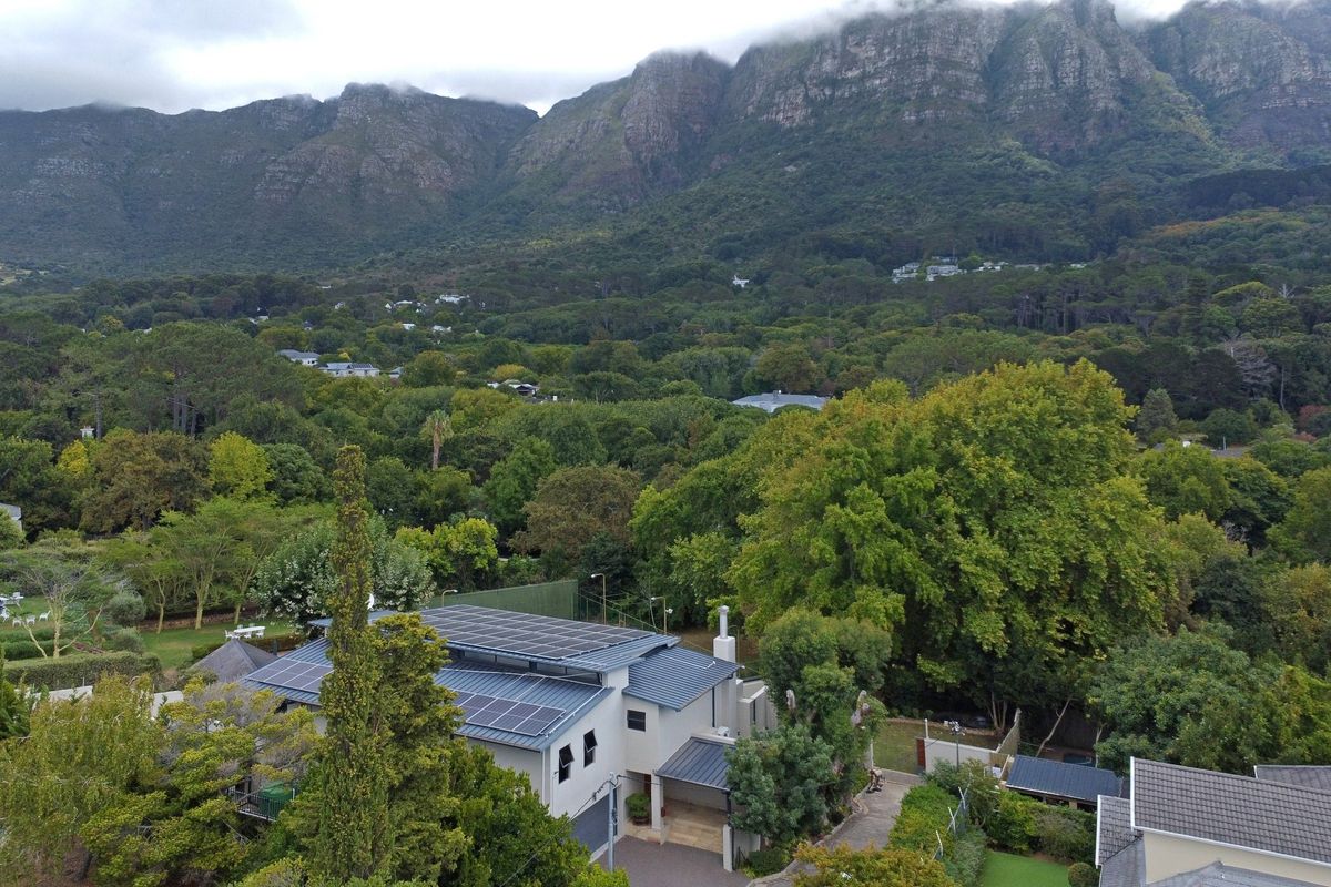 Aerial view of a residential property featuring a metal roof with integrated solar panels, set against a lush, mountainous landscape.