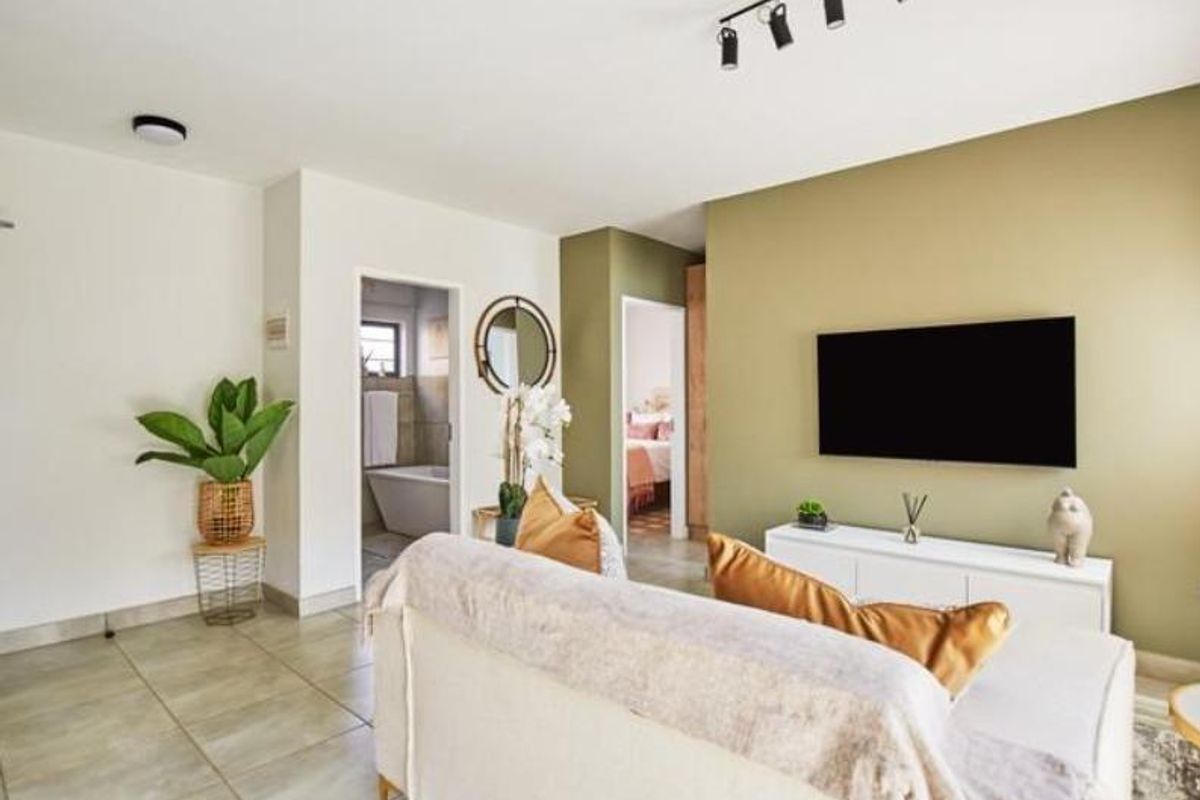 A bright and modern living room featuring tiled flooring, neutral walls with an olive accent wall, and track lighting.