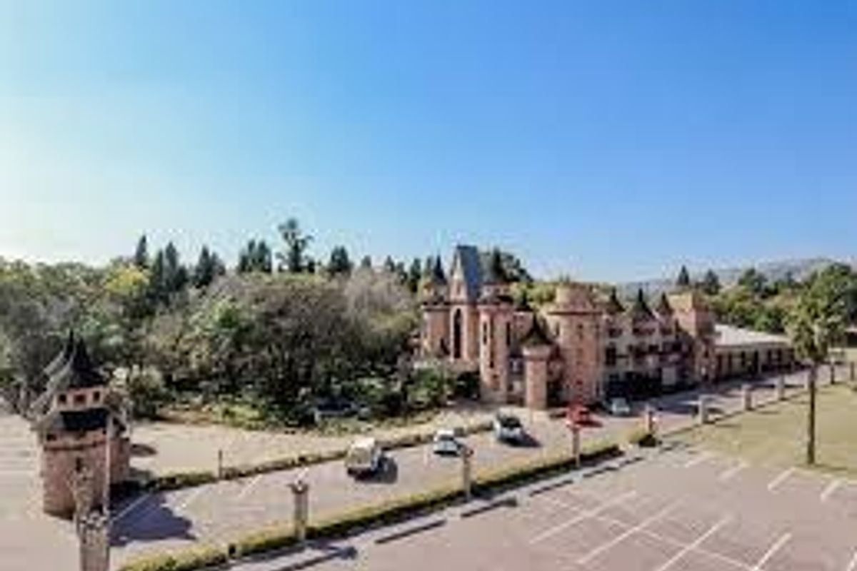 Aerial view of a unique castle-style commercial property featuring extensive landscaped grounds, turrets, and a large paved parking area.