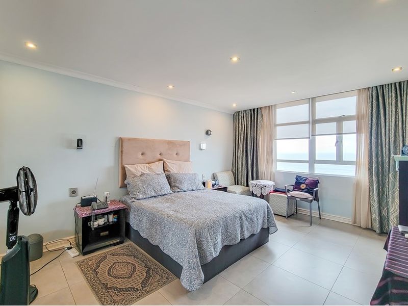A well-lit bedroom featuring tiled flooring, recessed downlights, and large windows offering natural light and ocean views.