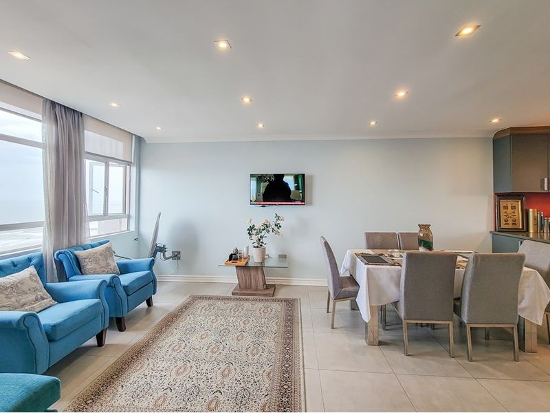 Spacious open-plan living and dining area featuring tiled floors, recessed lighting, and large windows with ocean views, seamlessly connected to a modern kitchen.
