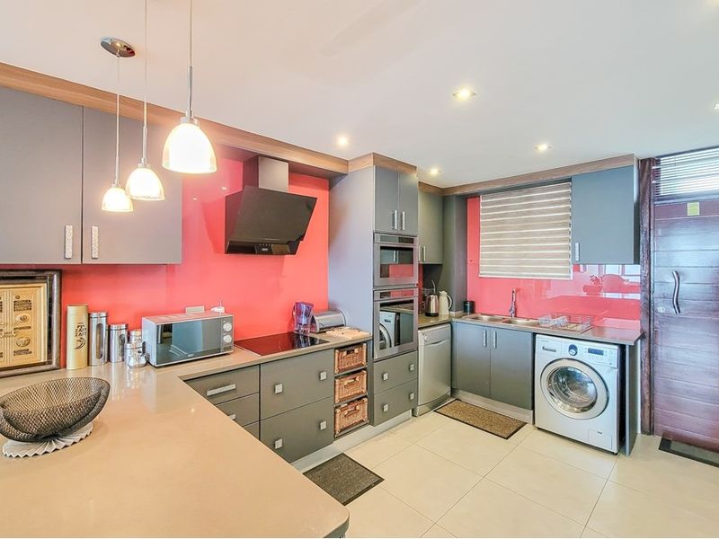 Modern kitchen featuring grey cabinetry, red glass splashback, stone countertops, and integrated appliances including an oven, microwave, and dishwasher.