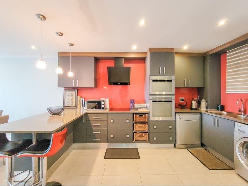 Modern kitchen featuring dark grey cabinetry, a vibrant red splashback, built-in oven, integrated appliances, and a functional breakfast bar with pendant lighting.