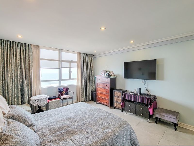 A spacious bedroom featuring tiled flooring, recessed lighting, and large windows with ocean views, offering a bright and comfortable living space.