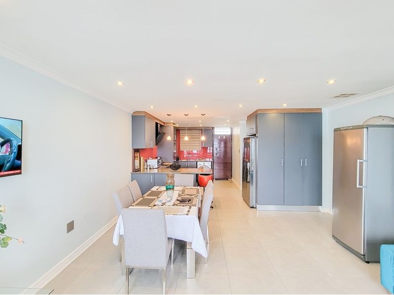 Open-plan living and dining area featuring tiled flooring, recessed lighting, and a modern kitchen with built-in cabinetry and a vibrant splashback.