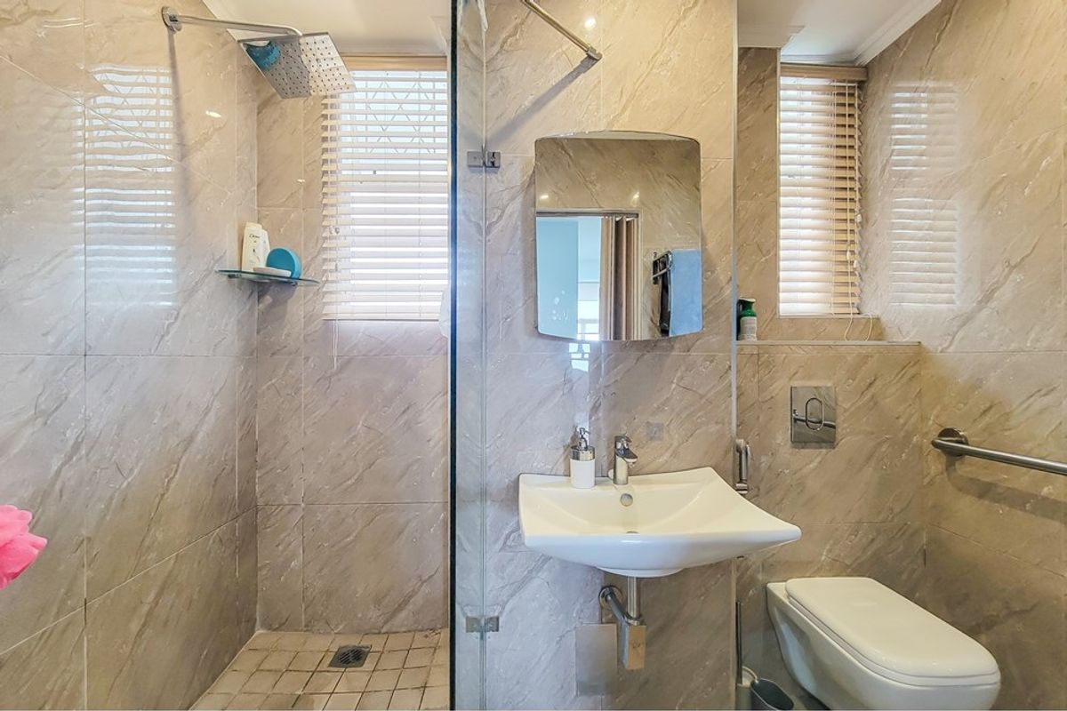 Modern bathroom featuring a walk-in shower with rain head, wall-mounted basin, and wall-hung toilet, finished with neutral marble-look wall tiles.