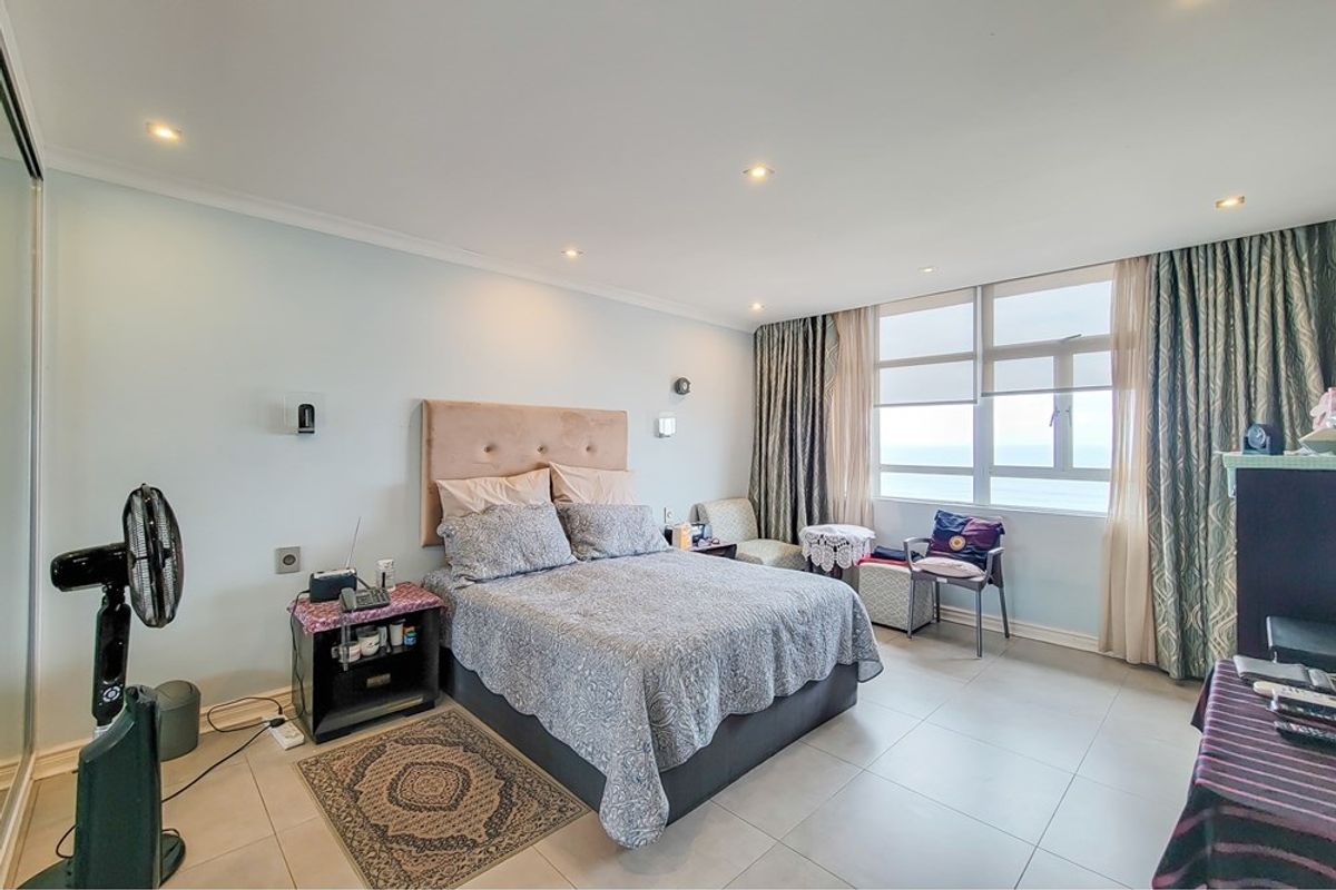 A well-lit bedroom featuring tiled flooring, recessed downlights, and large windows offering natural light and ocean views.