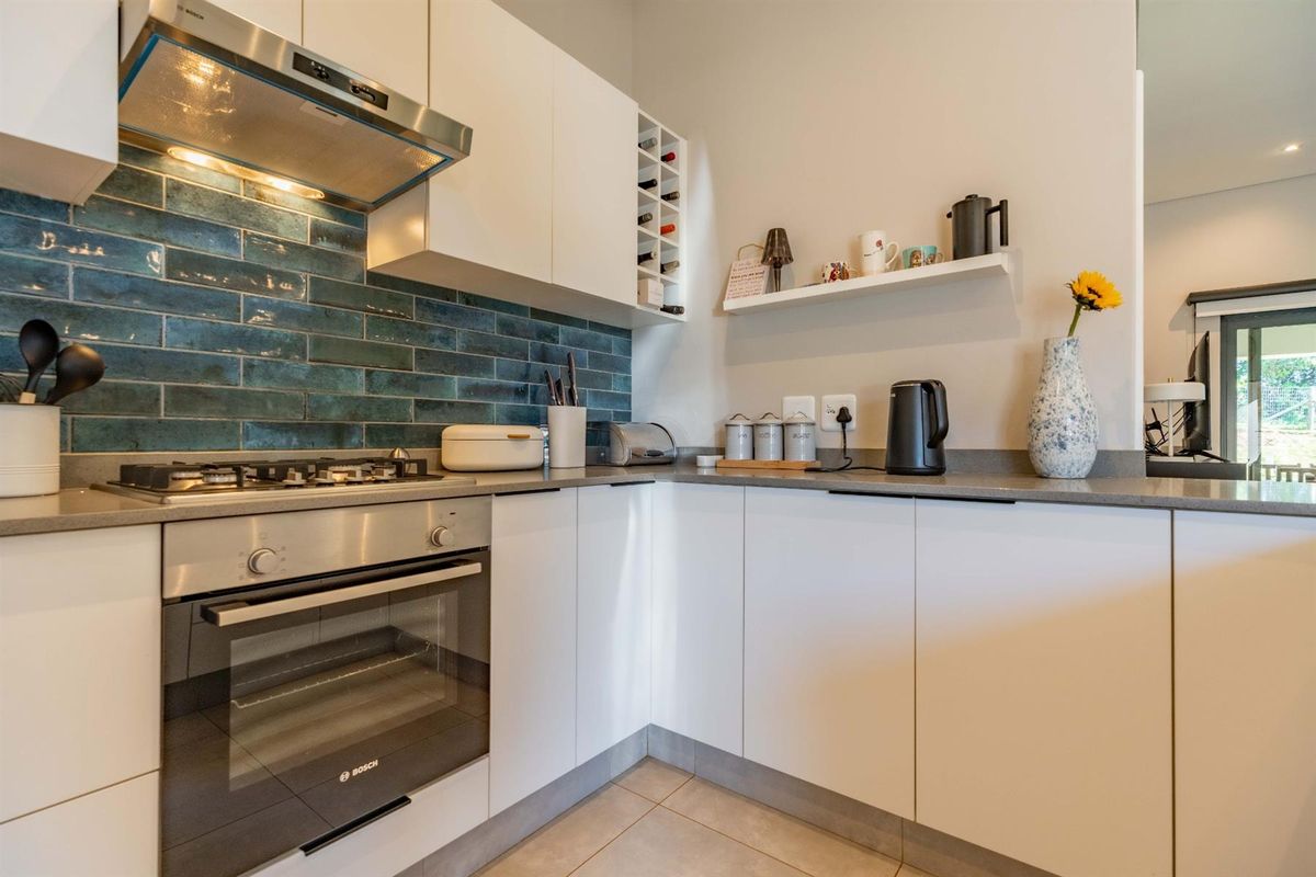 Modern kitchen featuring white cabinetry, stone countertops, a gas hob, built-in oven, stainless steel extractor fan, and a striking blue subway tile backsplash.