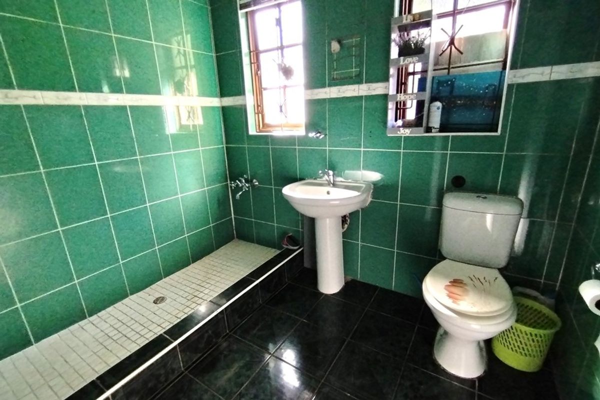 A dated bathroom featuring green wall tiles, a pedestal basin, a walk-in shower area, and a standard toilet.