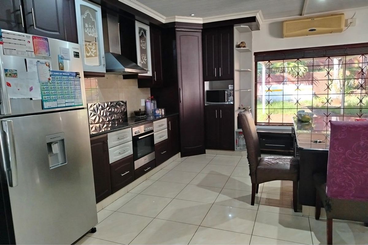 A functional kitchen featuring dark wood cabinetry, integrated oven and extractor fan, tiled flooring, and a window with security bars.