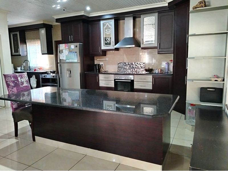 Spacious kitchen featuring dark wood cabinetry, granite countertops, a central island, built-in oven, extractor fan, and tiled flooring.