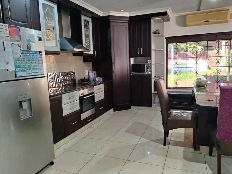 A functional kitchen featuring dark wood cabinetry, integrated oven and extractor fan, tiled flooring, and a window with security bars.