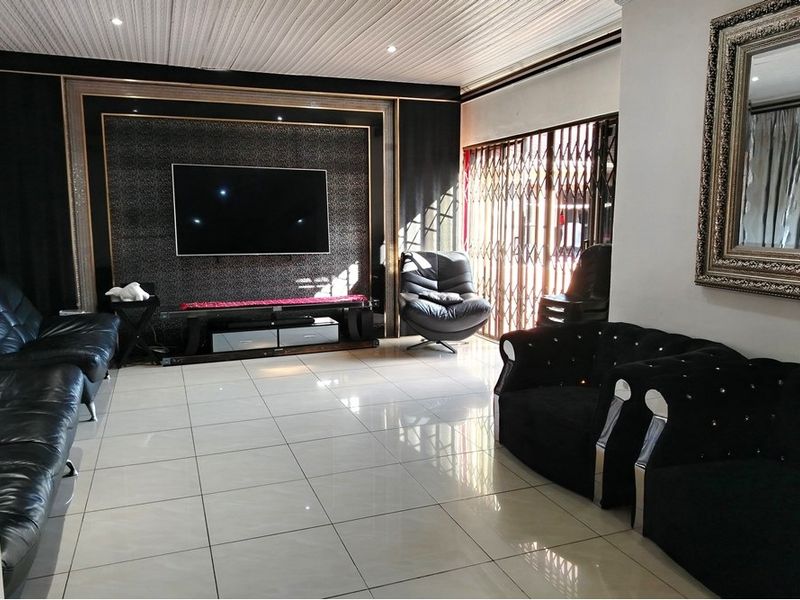 Spacious living room featuring large format floor tiles, a decorative feature wall with integrated lighting, and a security gate leading to the exterior.